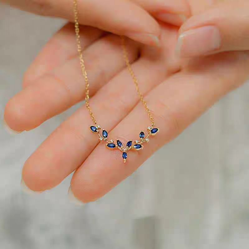 Gold necklace with blue stones held in a hand against a neutral background
