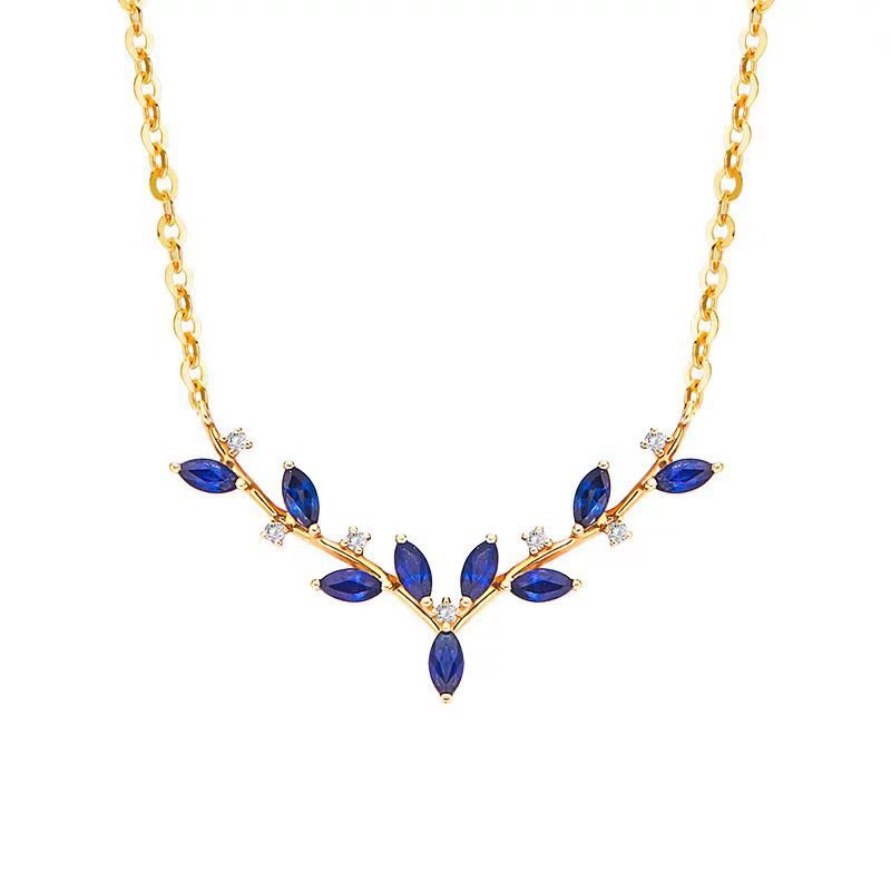 A gold necklace featuring a leaf-shaped pendant with marquise-cut blue gemstones and small clear accent stones, shown on a plain white background.