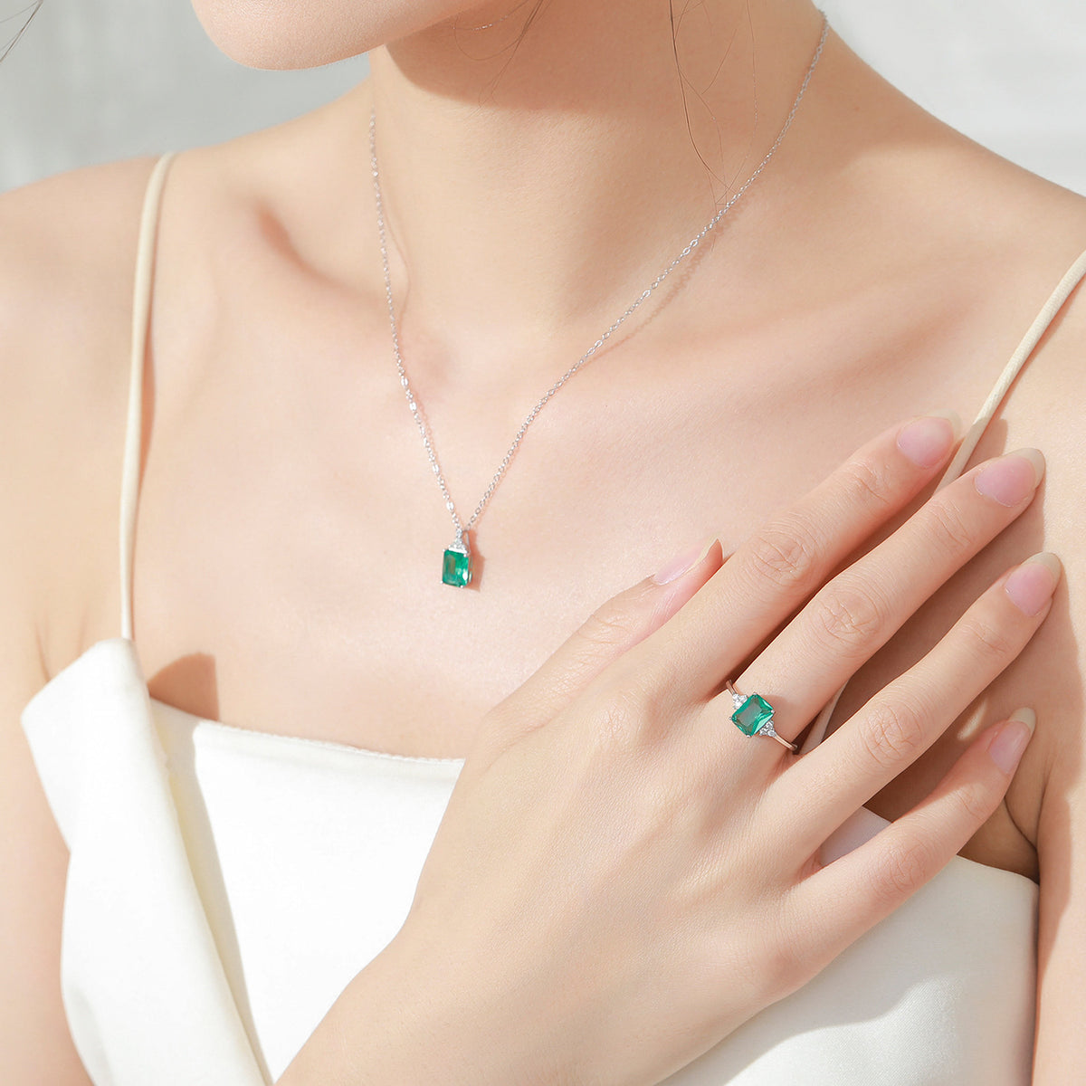 Woman wearing a silver necklace with a green gemstone pendant and matching ring on a plain background