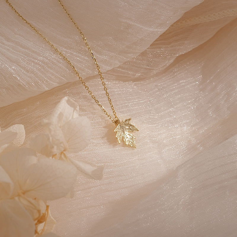 Gold leaf necklace on a soft beige fabric background