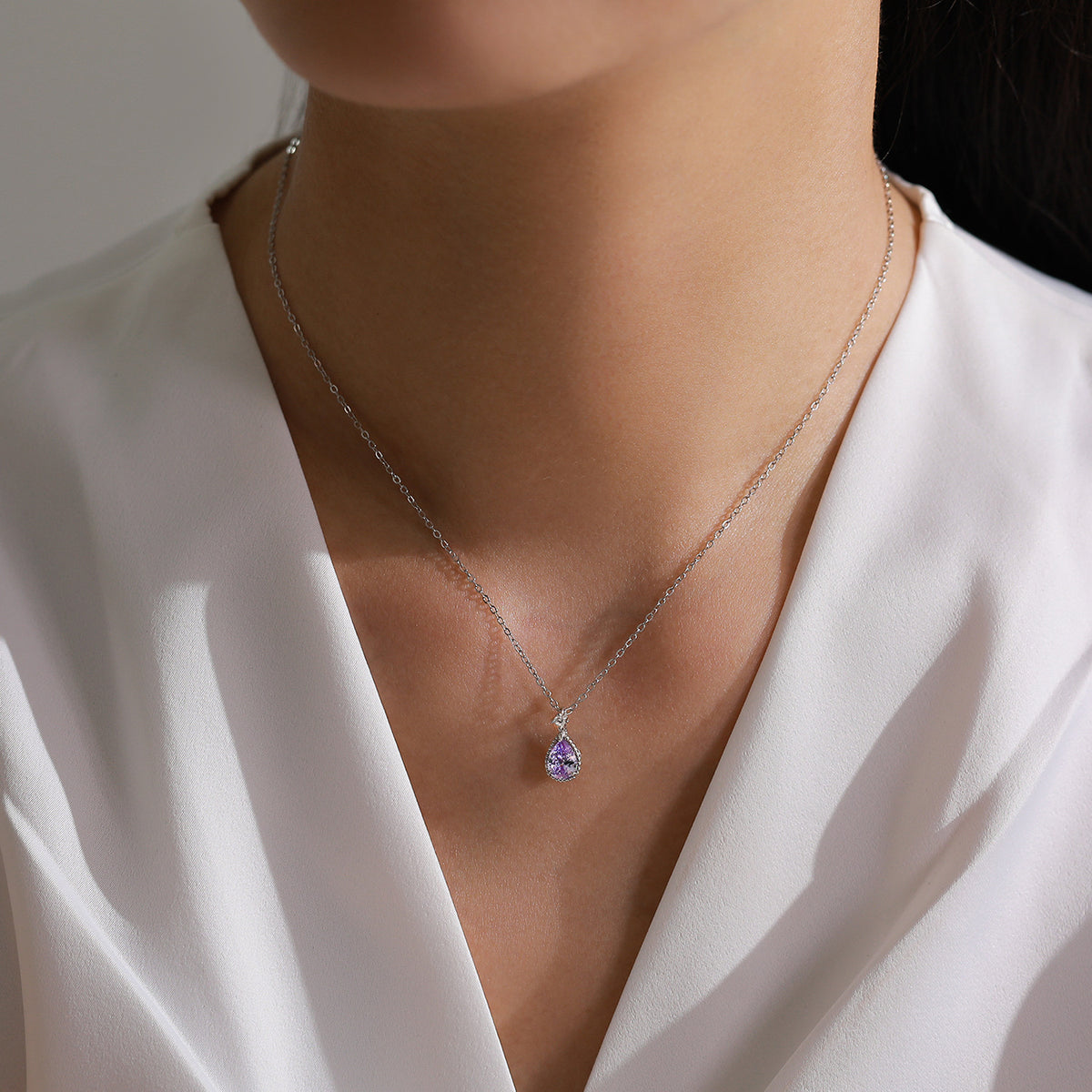 Necklace with a purple pendant worn by a person in a white outfit