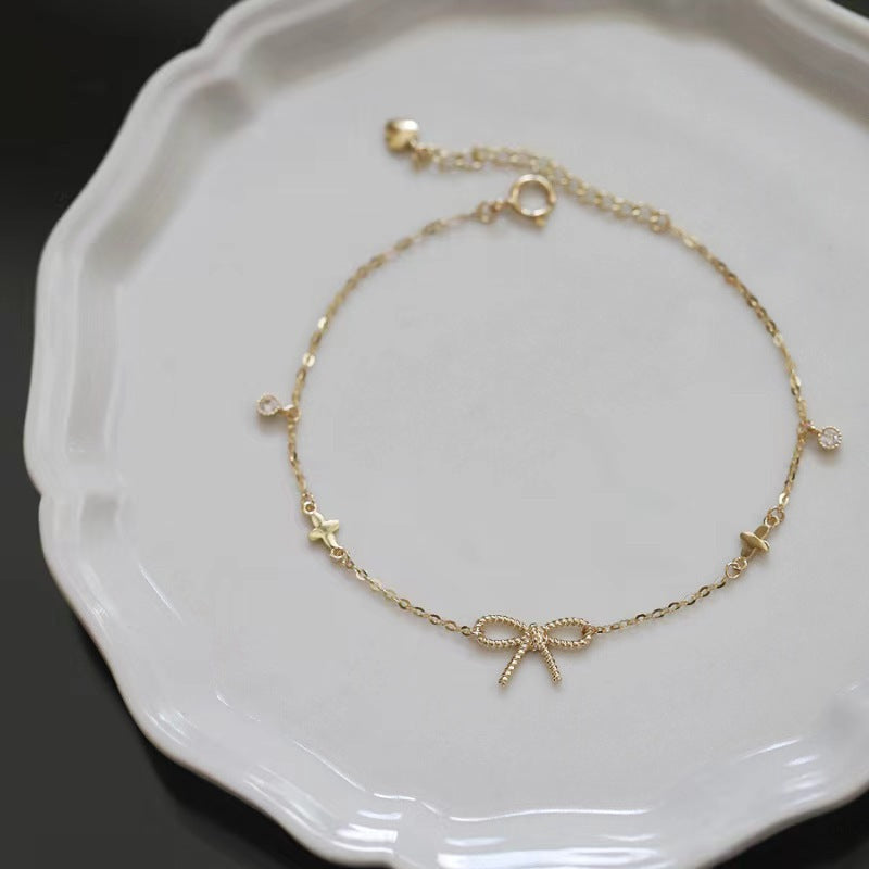 Gold bracelet with bow charm on a white plate