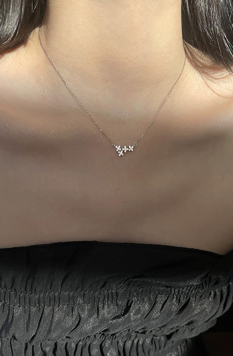 A delicate gold double-strand bracelet with a small flower charm and a star-shaped crystal accent, shown worn on a person's wrist with their hand resting behind it.