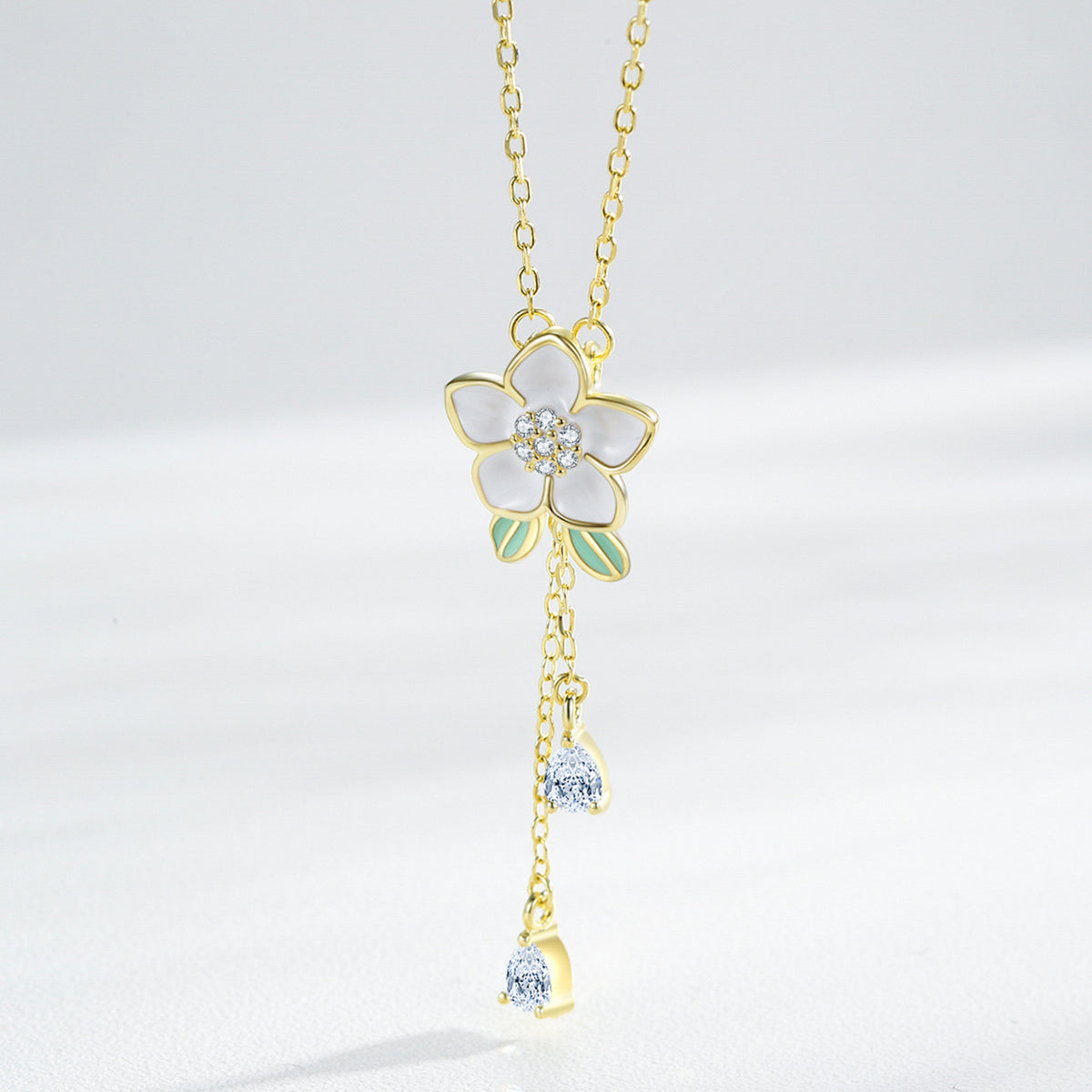A delicate gold double-strand bracelet with a small flower charm and a star-shaped crystal accent, shown worn on a person's wrist with their hand resting behind it.
